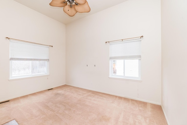 carpeted spare room featuring a wealth of natural light, visible vents, baseboards, and a ceiling fan