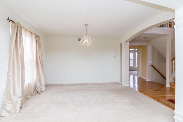 carpeted empty room with visible vents, stairway, arched walkways, an inviting chandelier, and ornate columns