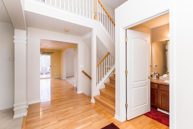 corridor featuring stairway, decorative columns, baseboards, and light wood-type flooring