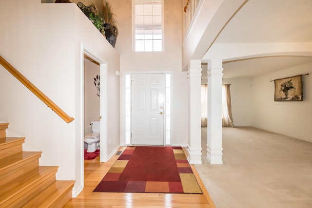 entryway featuring stairway, wood finished floors, decorative columns, arched walkways, and a towering ceiling