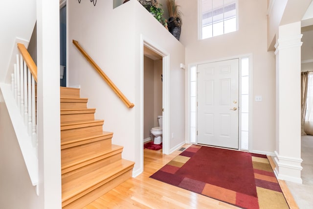 entryway with baseboards, stairs, a towering ceiling, wood finished floors, and ornate columns