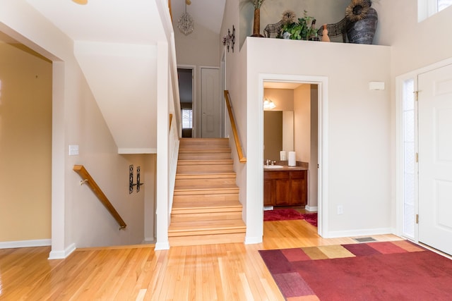 foyer entrance with a towering ceiling, stairs, baseboards, and hardwood / wood-style flooring