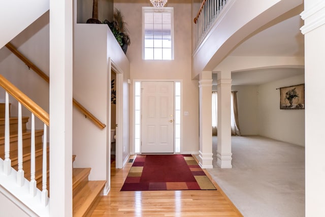 entrance foyer featuring stairway, a high ceiling, wood finished floors, arched walkways, and ornate columns