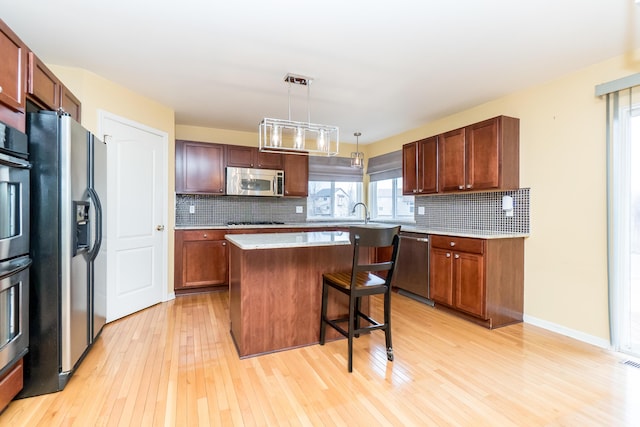 kitchen with a kitchen island, a breakfast bar, decorative backsplash, light wood-style floors, and appliances with stainless steel finishes