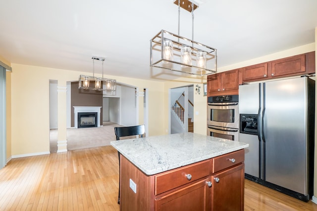 kitchen featuring light stone counters, light wood finished floors, a fireplace, hanging light fixtures, and appliances with stainless steel finishes