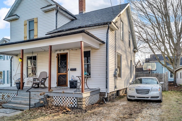 view of front of house featuring fence, covered porch, roof with shingles, and a chimney