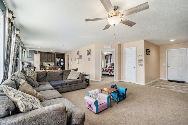 living area with visible vents, a ceiling fan, a textured ceiling, baseboards, and light colored carpet