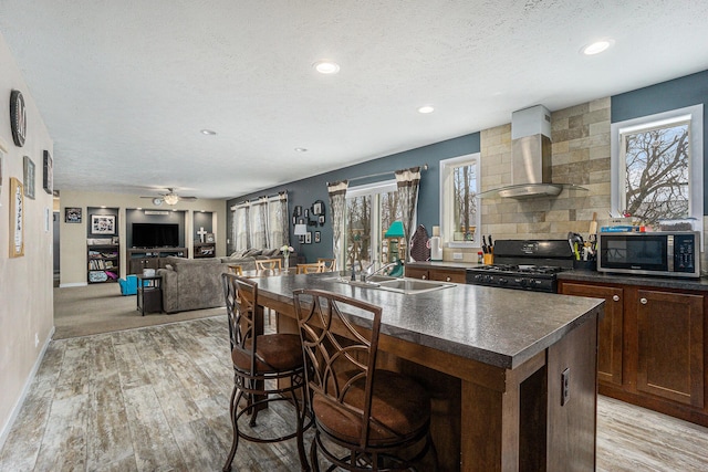 kitchen with stainless steel microwave, plenty of natural light, dark countertops, wall chimney range hood, and black range with gas stovetop