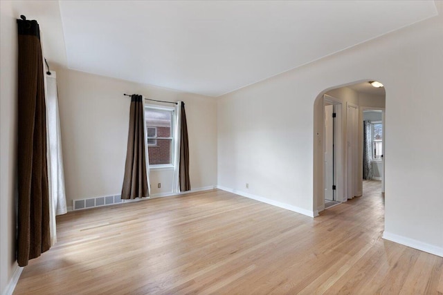 empty room with arched walkways, visible vents, light wood-style flooring, and a wealth of natural light