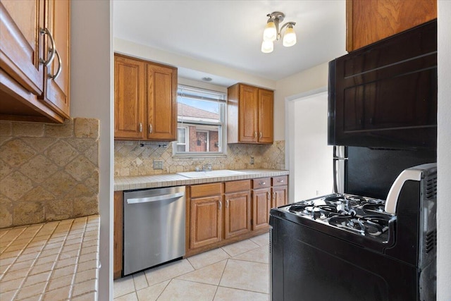 kitchen featuring tile countertops, light tile patterned flooring, a sink, gas range oven, and dishwasher