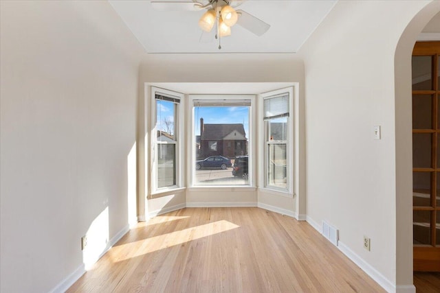 empty room with light wood-type flooring, visible vents, a ceiling fan, arched walkways, and baseboards