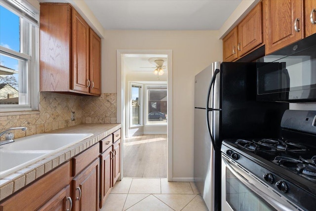 kitchen featuring a sink, tasteful backsplash, stainless steel range with gas cooktop, brown cabinetry, and light tile patterned floors