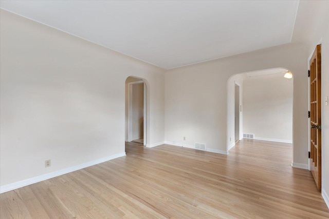 empty room with light wood-style floors, arched walkways, visible vents, and baseboards