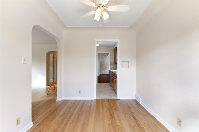 unfurnished room with visible vents, arched walkways, ceiling fan, and light wood finished floors