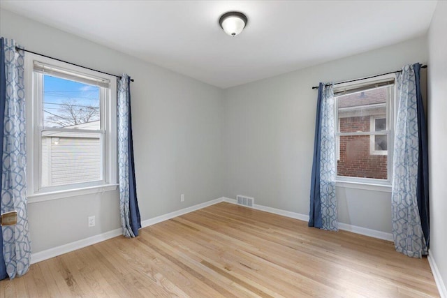 unfurnished room with wood finished floors, visible vents, and baseboards