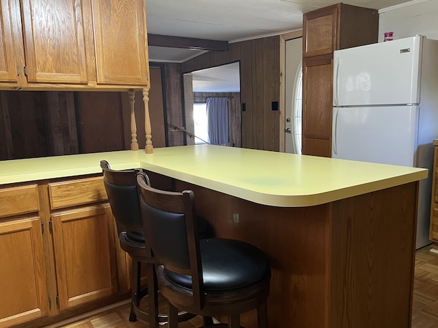 kitchen featuring a kitchen breakfast bar, freestanding refrigerator, wood walls, brown cabinetry, and light countertops