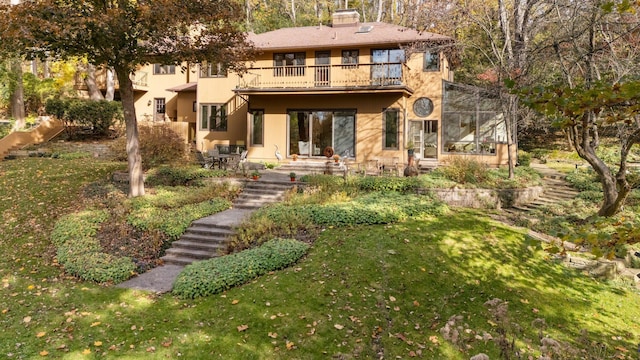 rear view of property with stairway, stucco siding, a chimney, a balcony, and a yard