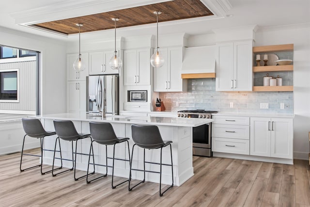 kitchen with custom exhaust hood, an island with sink, light countertops, and appliances with stainless steel finishes