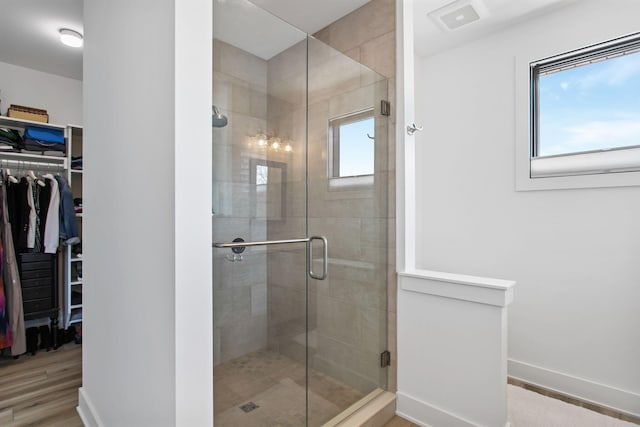 full bathroom featuring a spacious closet, a shower stall, baseboards, and wood finished floors