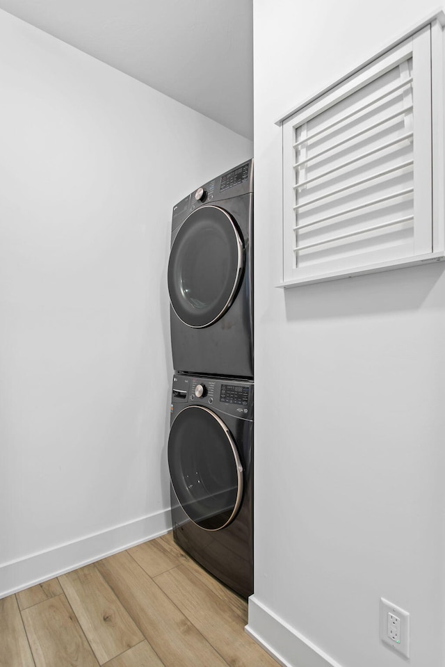 laundry area with baseboards, wood finished floors, laundry area, and stacked washing maching and dryer