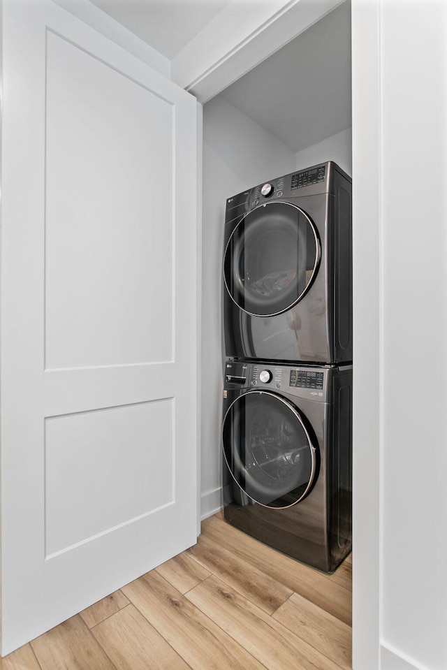 laundry area with laundry area, wood finished floors, and stacked washer / drying machine