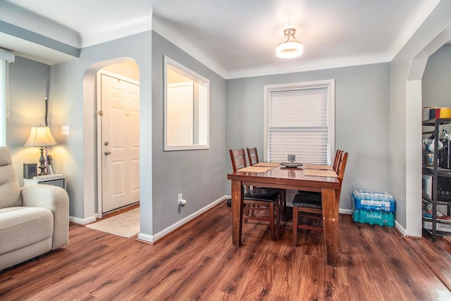 dining area featuring arched walkways, baseboards, and wood finished floors