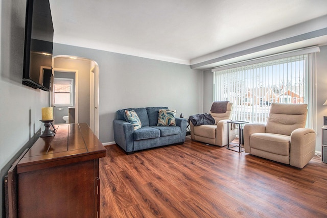 living room featuring arched walkways, baseboards, and dark wood-style flooring