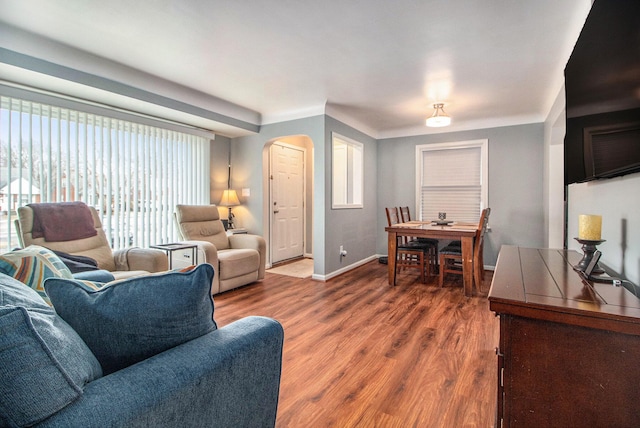 living area with arched walkways, baseboards, and wood finished floors