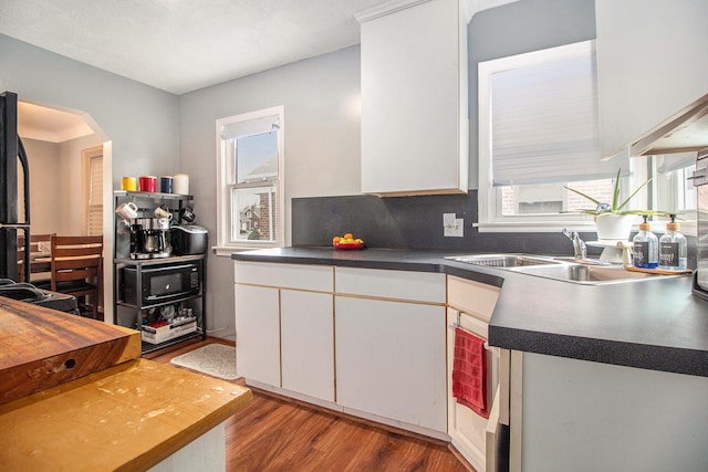 kitchen with wood finished floors, arched walkways, a sink, white cabinets, and dark countertops