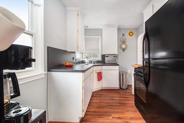 kitchen featuring dark wood-style flooring, a sink, black appliances, white cabinets, and dark countertops