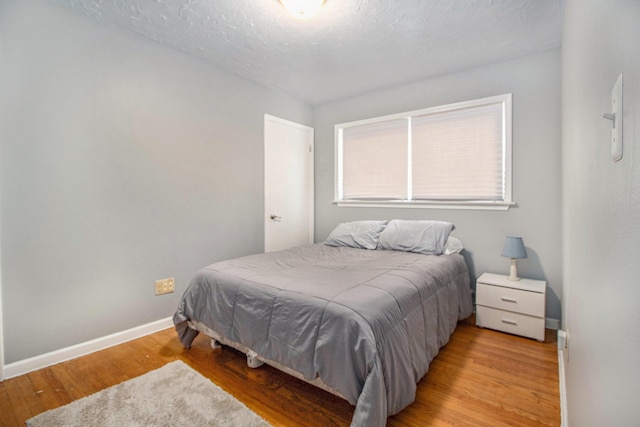 bedroom with a textured ceiling, baseboards, and light wood-style floors