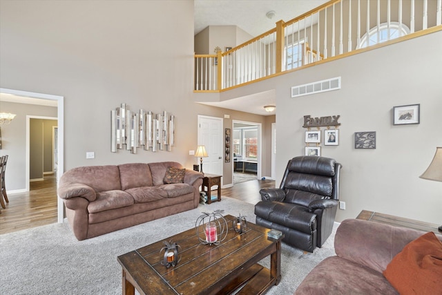 carpeted living room with a notable chandelier, visible vents, a towering ceiling, and wood finished floors