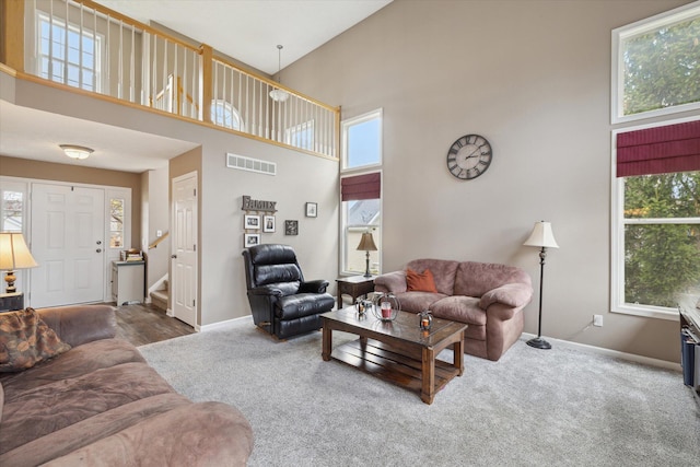 carpeted living room with visible vents, a healthy amount of sunlight, a towering ceiling, and stairs