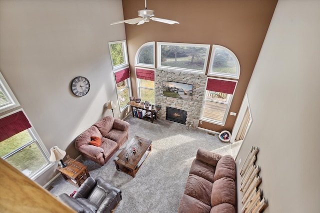 carpeted living room featuring a high ceiling, a stone fireplace, and a ceiling fan