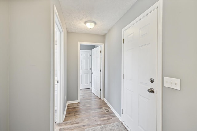 hall with light wood-style floors, baseboards, and a textured ceiling