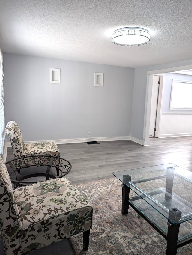 living room featuring visible vents, wood finished floors, baseboards, and a textured ceiling