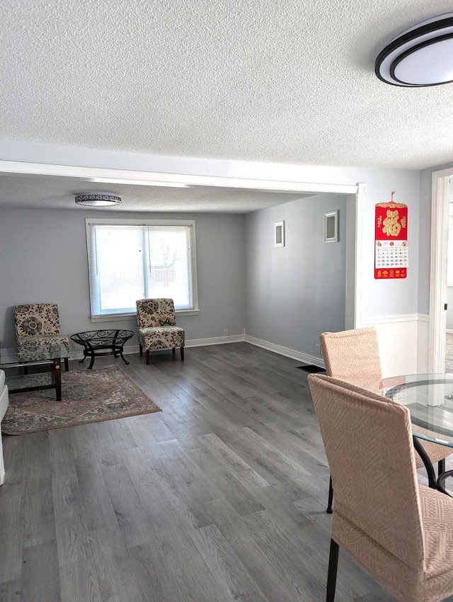 living area with visible vents, a textured ceiling, baseboards, and wood finished floors