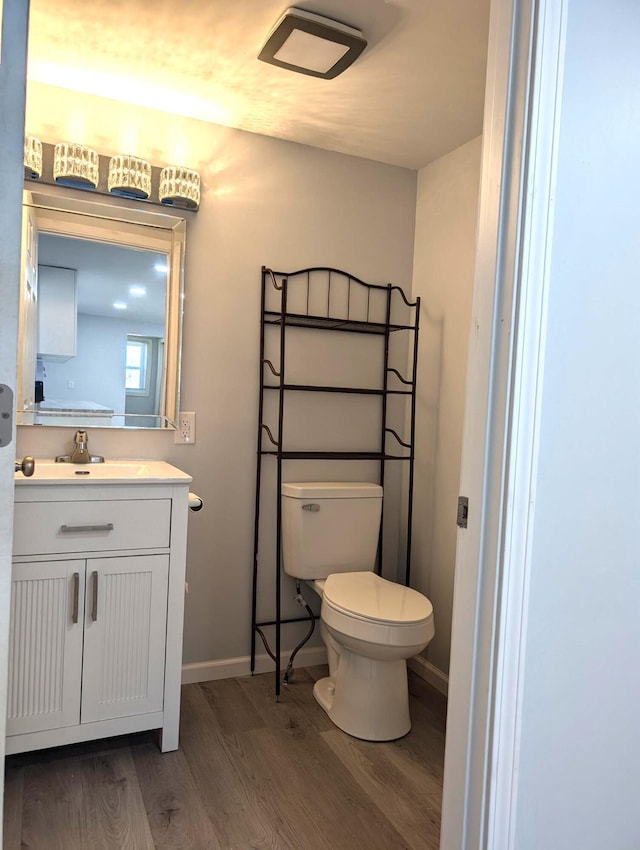 half bath with baseboards, toilet, wood finished floors, and vanity