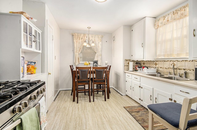 kitchen with decorative backsplash, gas stove, white cabinetry, and a sink