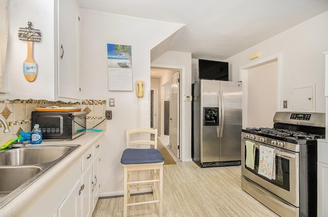 kitchen with a sink, stainless steel appliances, white cabinetry, light wood-type flooring, and backsplash