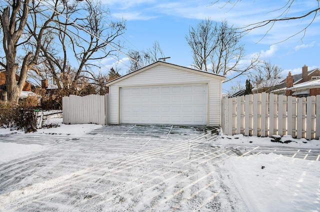 snow covered garage with a detached garage and fence