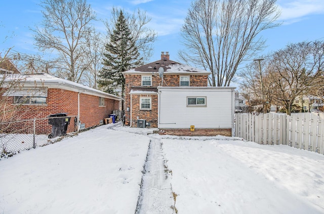 snow covered back of property featuring fence, brick siding, and a chimney