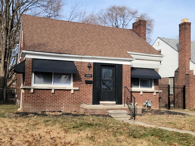 view of front facade featuring brick siding, a shingled roof, and fence