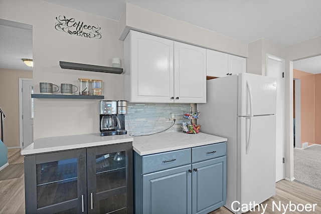 kitchen with light wood-type flooring, open shelves, freestanding refrigerator, white cabinetry, and tasteful backsplash