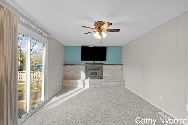 unfurnished living room with carpet flooring, baseboards, a wood stove, and ceiling fan