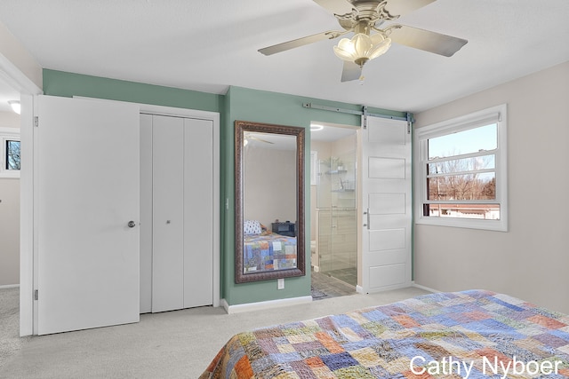 carpeted bedroom featuring a barn door, a ceiling fan, a closet, and connected bathroom