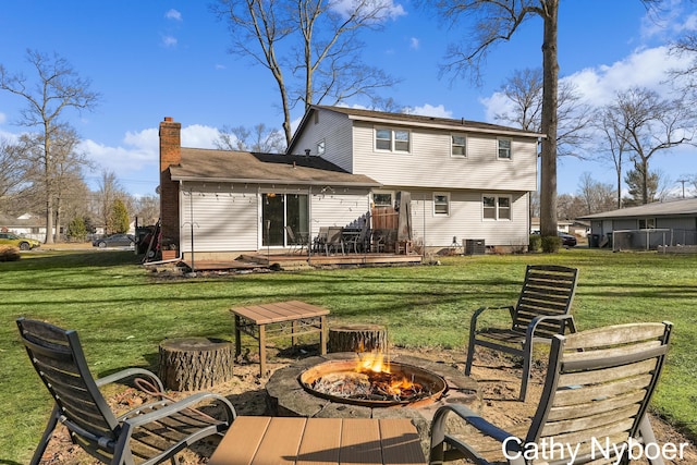 back of property with a chimney, a lawn, a fire pit, and a deck