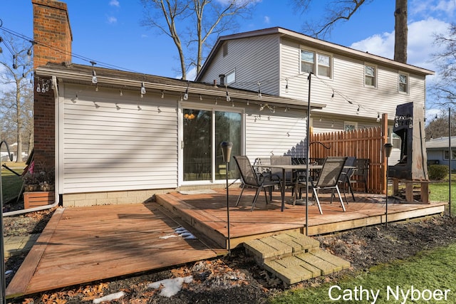 back of house featuring brick siding, a chimney, a deck, and fence