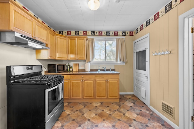 kitchen with visible vents, a sink, wood walls, under cabinet range hood, and appliances with stainless steel finishes