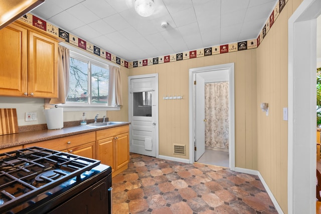 kitchen with black gas range oven, visible vents, baseboards, wood walls, and a sink